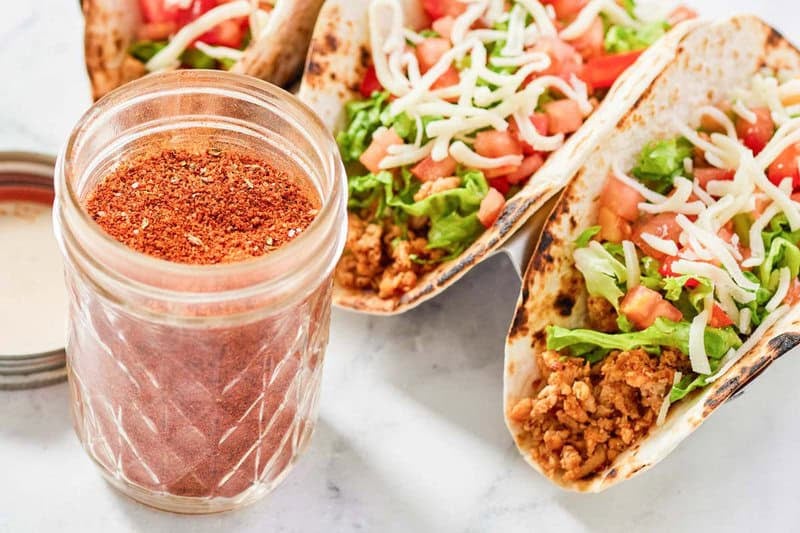 Homemade chicken taco seasoning in a jar and three chicken tacos.