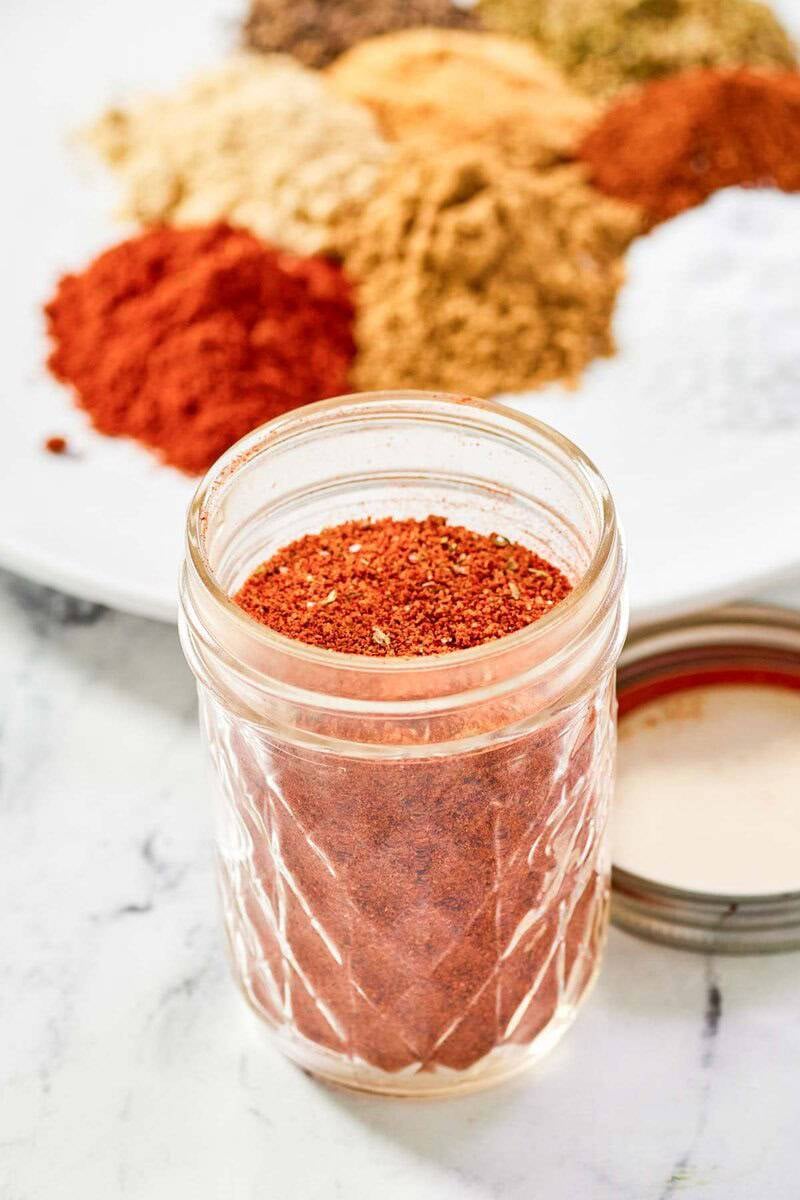 Homemade chicken taco seasoning in a mason jar and spices on a plate behind it.