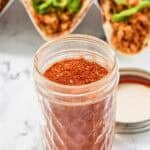 Homemade chicken taco seasoning in a jar and chicken tacos behind it.