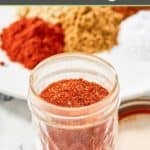 Homemade chicken taco seasoning in a glass jar and spices on a plate behind it.