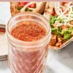 Homemade chicken taco seasoning blend in a small glass jar and chicken tacos by it.