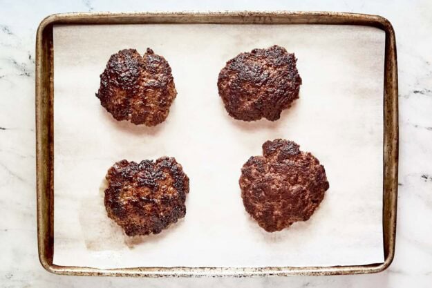 Four cooked burger patties on a tray.