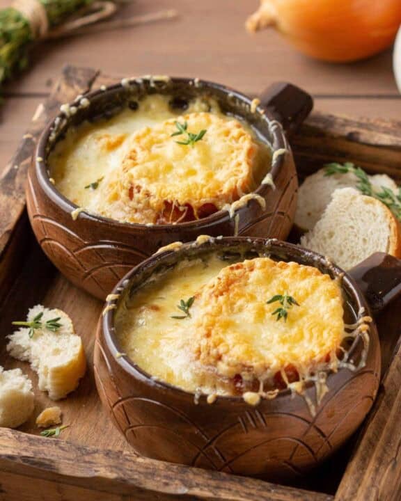 Bowls of homemade classic French onion soup on a wood tray.