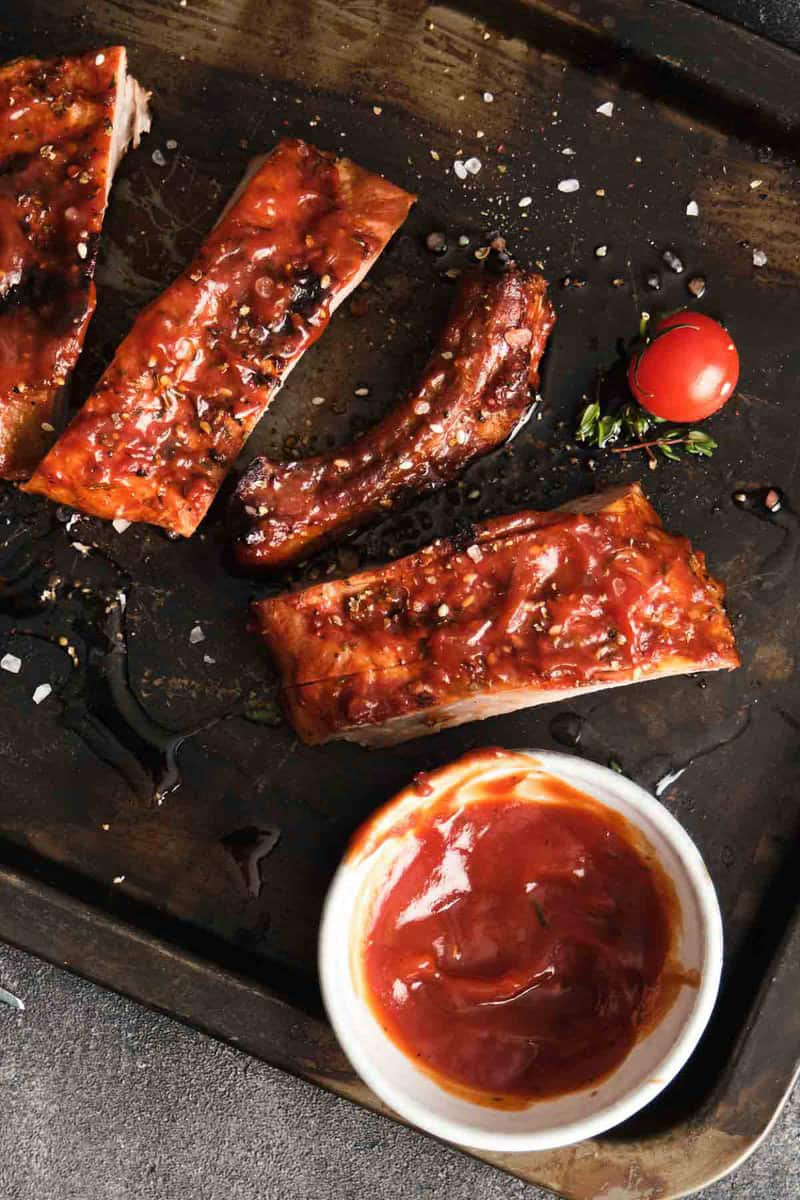 Homemade St. Louis style bbq sauce on pork ribs and in a small cup.