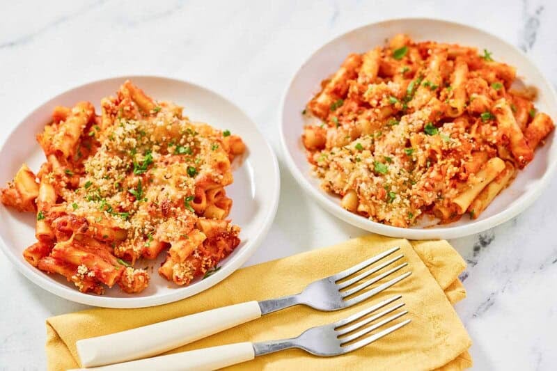 Copycat Olive Garden five cheese ziti al forno on two plates and two forks on a cloth napkin.