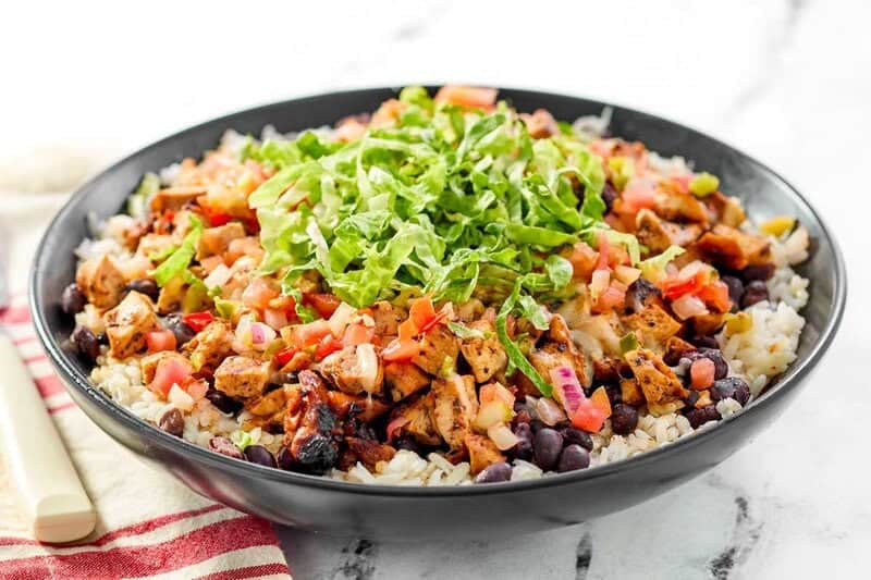 A rice bowl with copycat chipotle chicken, pico de gallo, black beans, and lettuce.