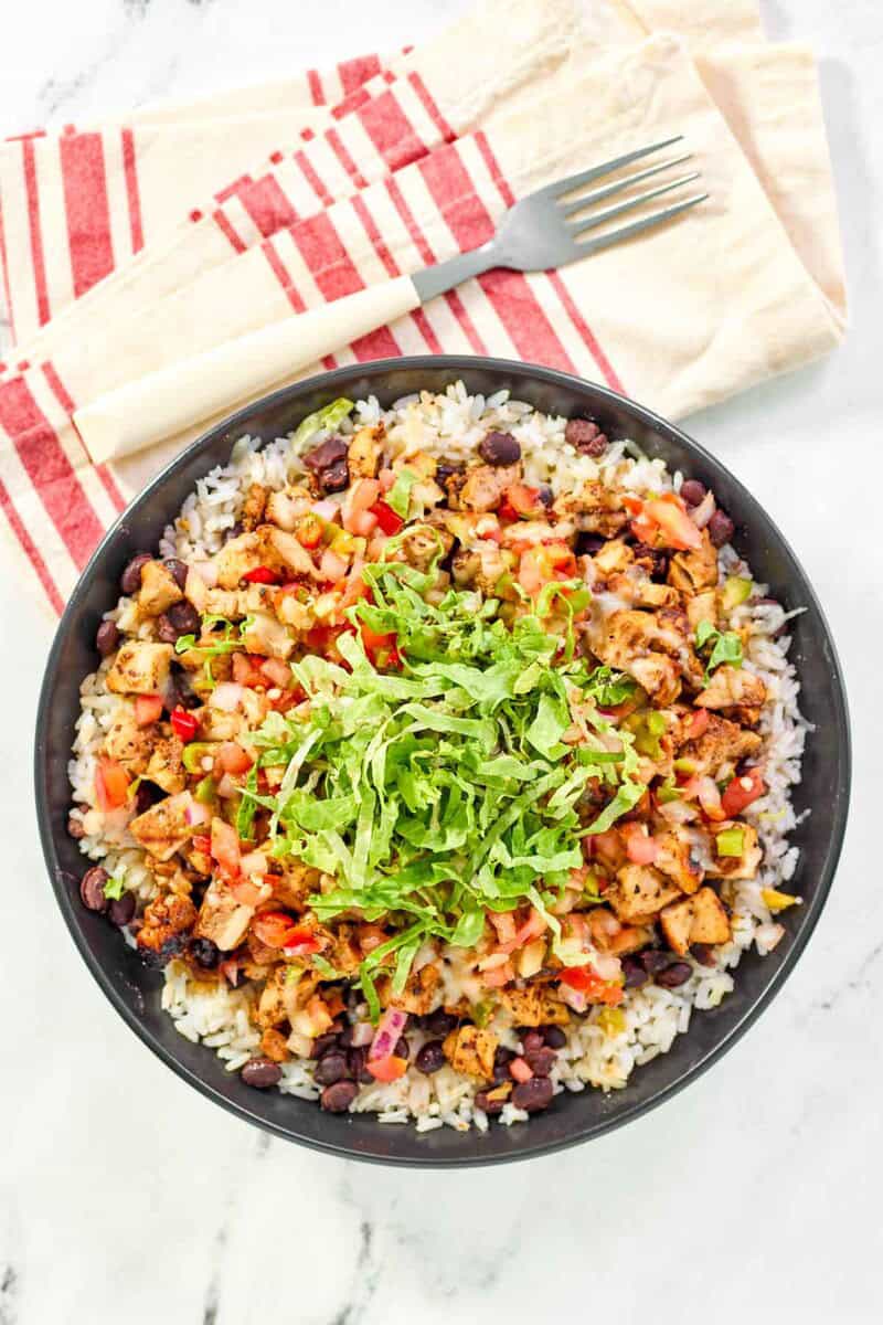 A rice bowl with copycat chipotle honey chicken, beans, pico de gallo, and lettuce.