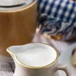 Homemade French vanilla coffee creamer in a small pitcher next to a cup of coffee.