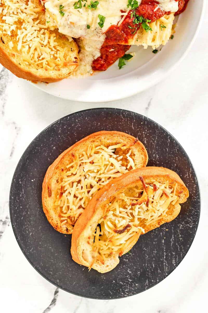 Copycat Marie Callender's garlic toast slices on a plate and with lasagna.