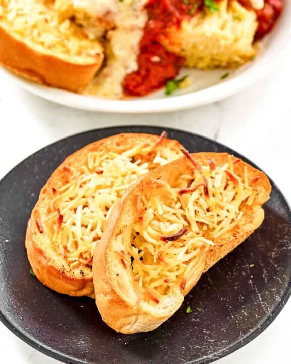 Slices of copycat Marie Callender's garlic toast on a plate and with lasagna.