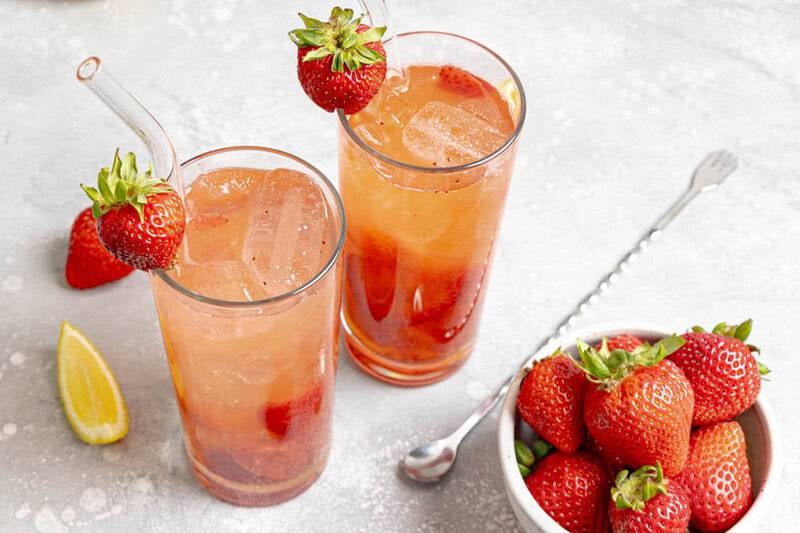 Copycat Red Robin freckled lemonade in two glasses and a bowl of strawberries.