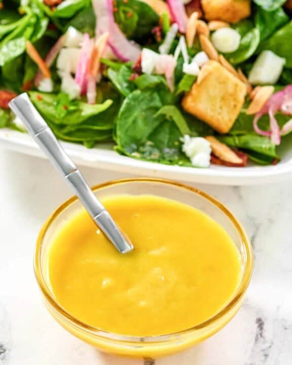Copycat Simon and Seafort's mustard dressing in a small bowl and a salad behind it.