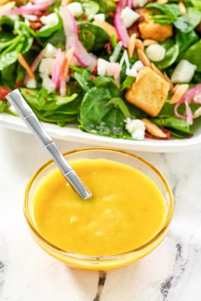 Copycat Simon and Seafort's mustard dressing in a small bowl and a salad behind it.