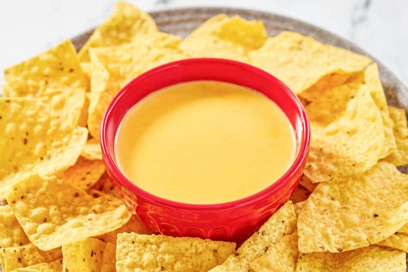 Copycat Taco Bell nacho cheese in a bowl and tortilla chips around it on a platter.