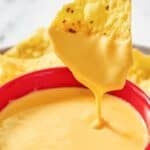 A bowl of homemade Taco Bell nacho cheese sauce and a chip being dipped in it.