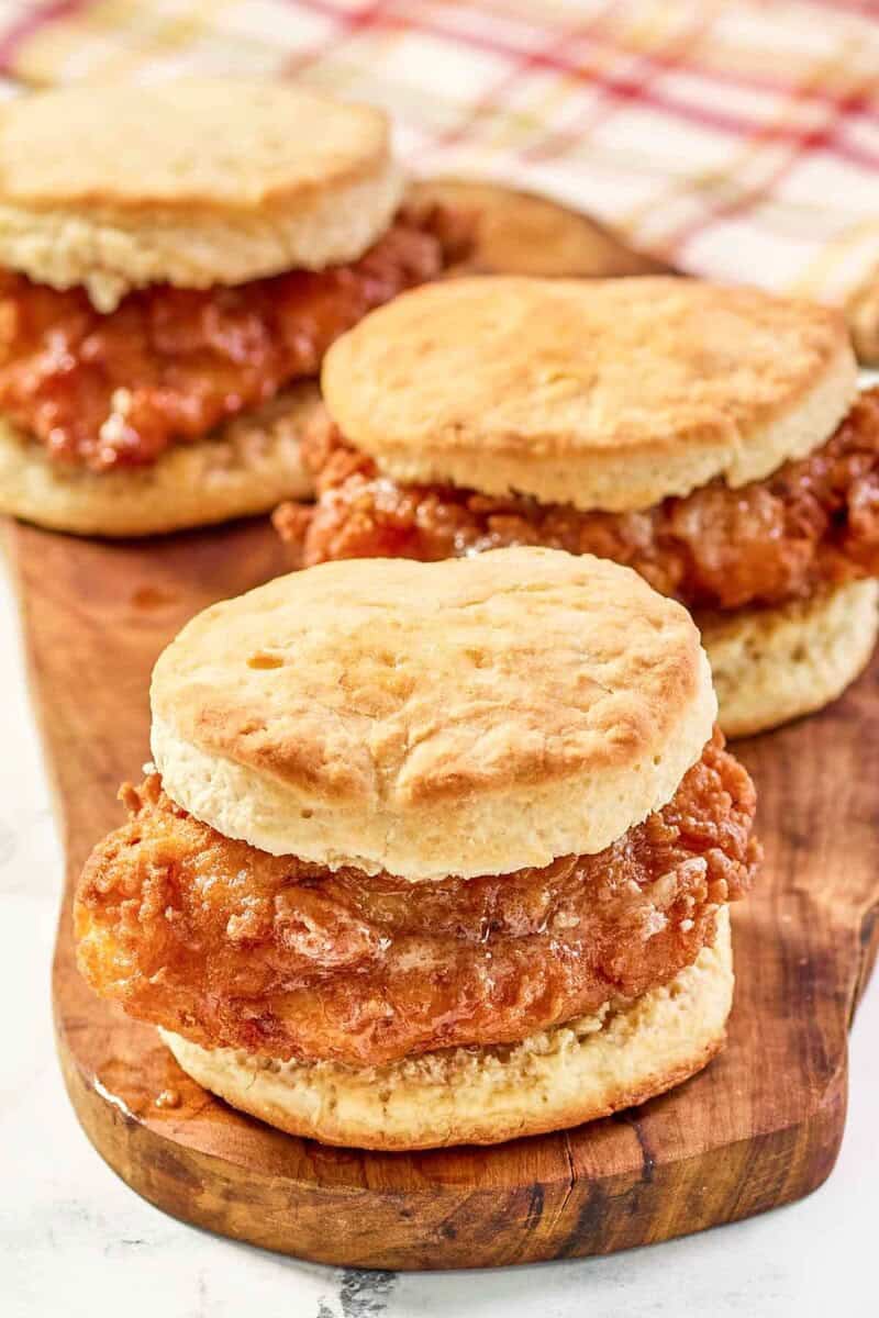 Three copycat Wendy's honey butter chicken biscuit sandwiches on a wood board.