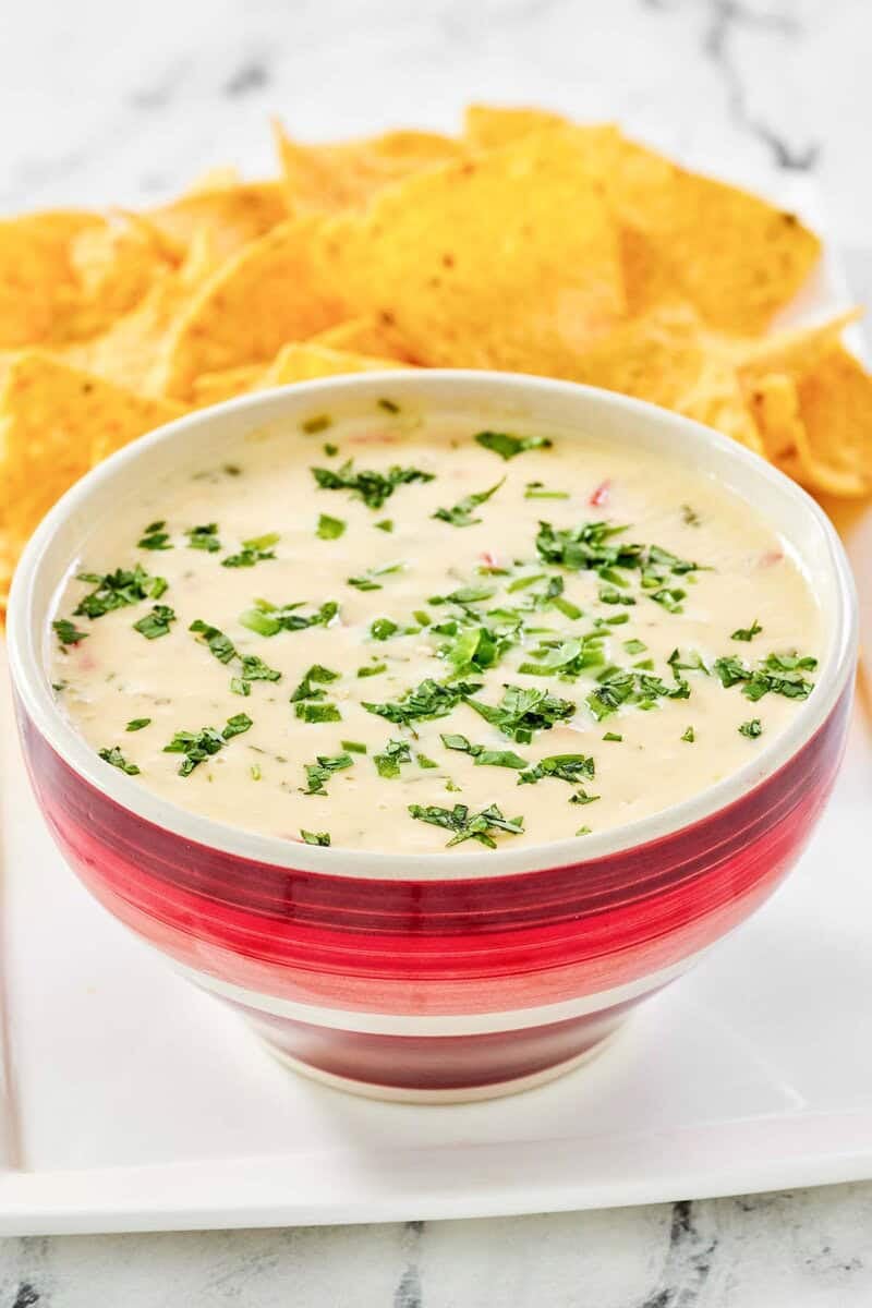 Copycat Applebee's queso blanco in a bowl on a platter with tortilla chips.