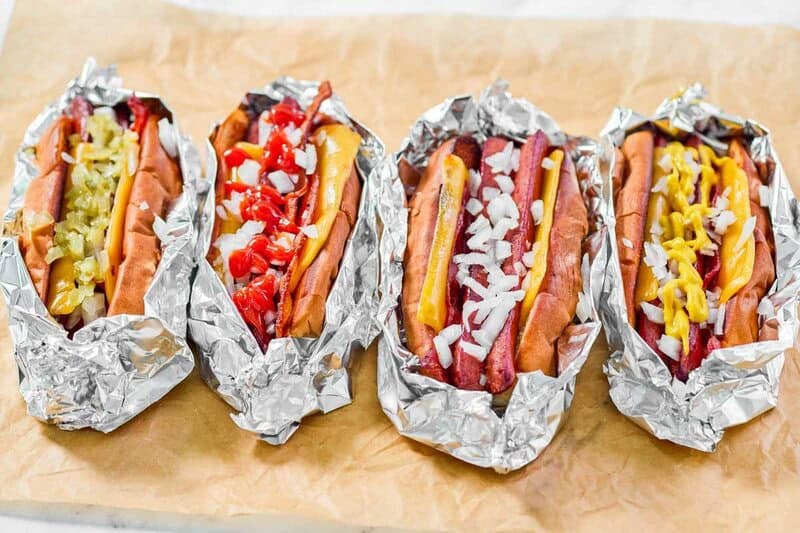 Four copycat Five Guys hot dogs with various toppings on parchment paper.
