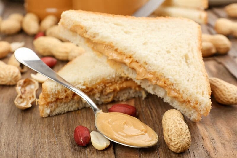 Homemade peanut butter on a spoon, peanuts, and peanut butter sandwich.