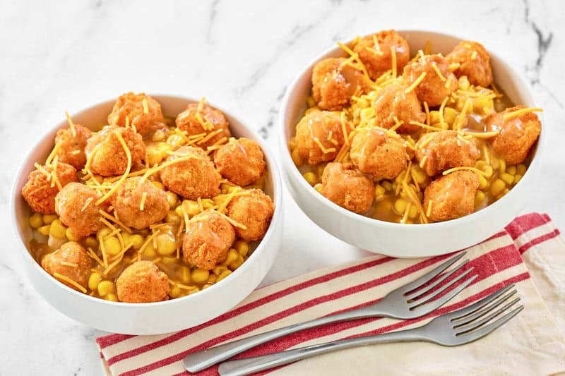 Two servings of copycat KFC famous bowl with mashed potatoes, gravy, corn, and cheese.