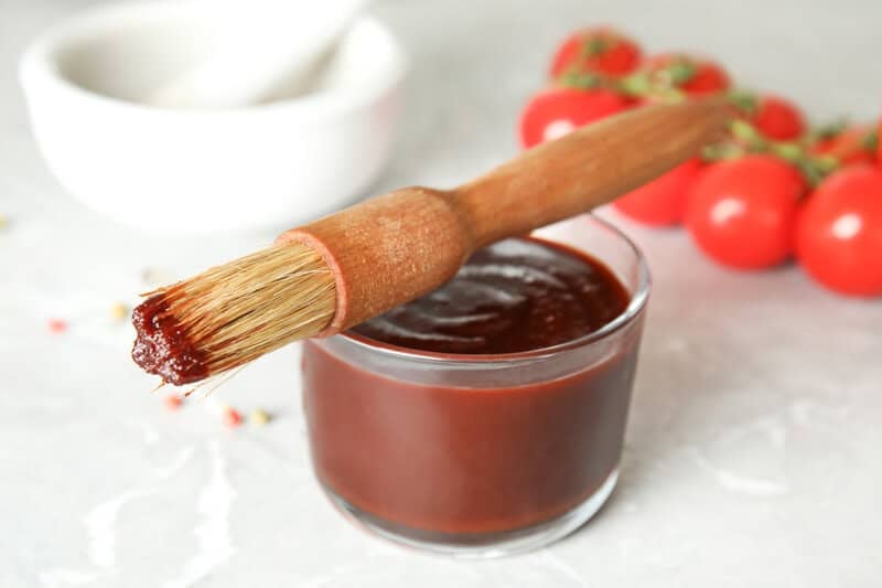 A bowl of copycat Swiss Chalet BBQ sauce and a basting brush on top of it.