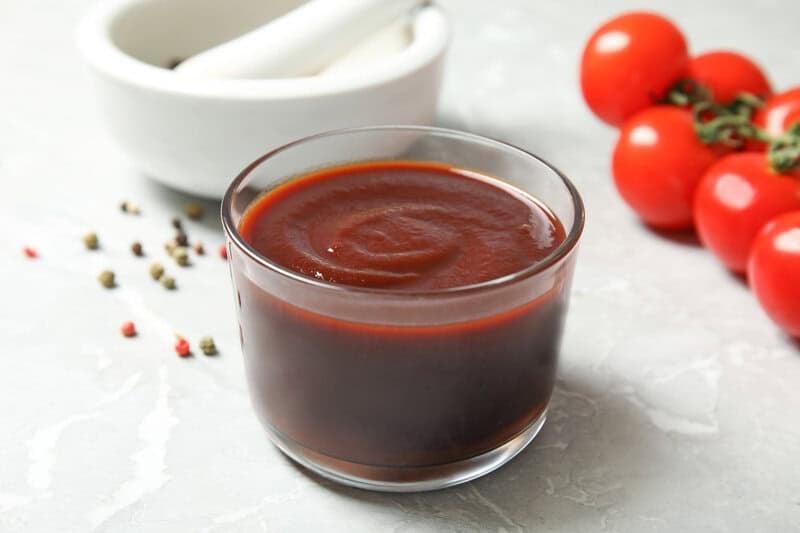 A small bowl of copycat Swiss Chalet BBQ sauce, tomatoes, and peppercorns.