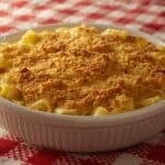 A retro Pyrex casserole dish filled with tuna noodle casserole sitting on a plaid tablecloth.