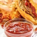 Homemade Arby's red ranch sauce in a bowl in front of roast beef sandwiches.