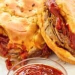 Copycat Arby's red ranch sauce in a bowl and two roast beef sandwiches behind it.