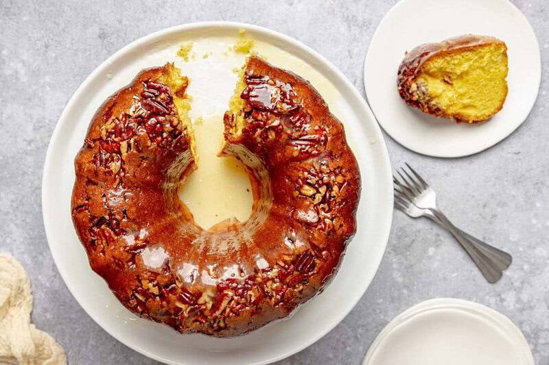 An overhead view of a glazed pecan rum cake on a platter with one slice removed. The slice sits on a separate small plate.