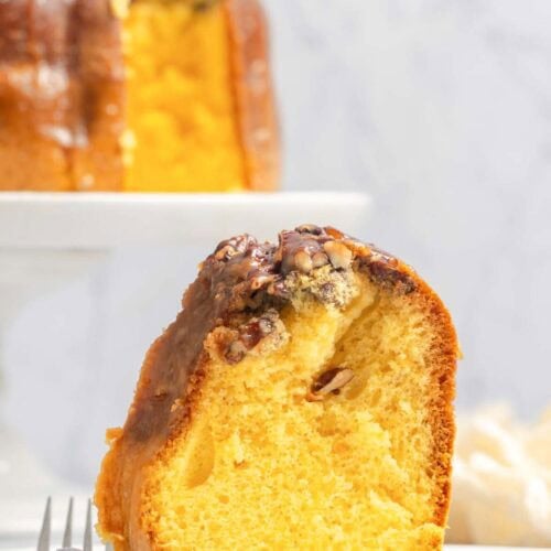 A slice of Bacardi rum cake and the cake behind it on a cake stand.
