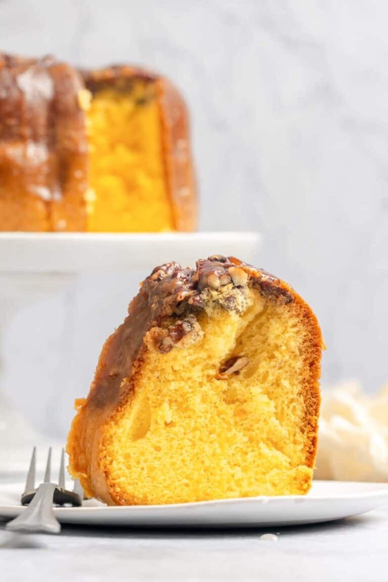A slice of Bacardi rum cake and the cake behind it on a cake stand.