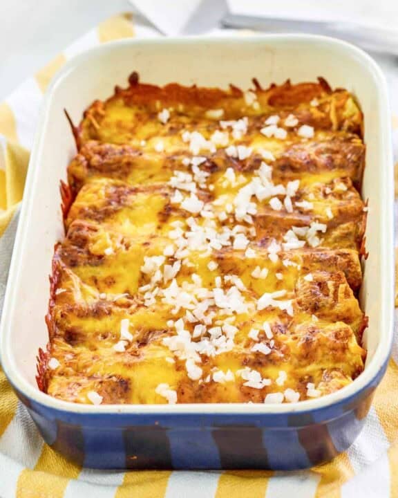 Copycat El Chico cheese enchiladas in a baking dish and a spatula behind it.
