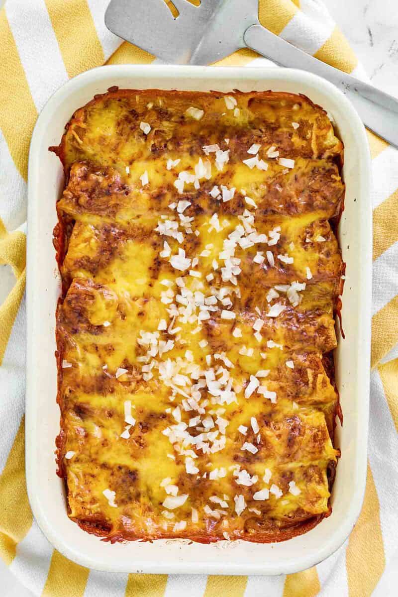 Copycat El Chico cheese enchiladas in a baking dish on a kitchen towel.