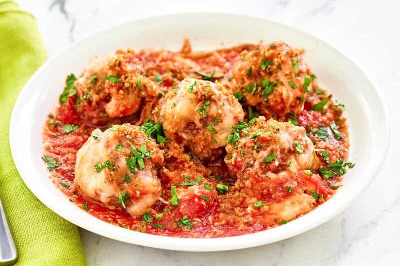 Overhead view of a bowl of Olive Garden meatball parmigiana. The meatballs are in sauce and topped with breadcrumbs and fresh parsley.