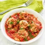 Copycat Olive Garden meatballs parmigiana and a fork on a napkin behind it.