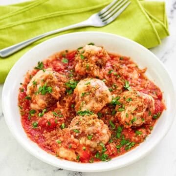 Copycat Olive Garden meatballs parmigiana and a fork on a napkin behind it.