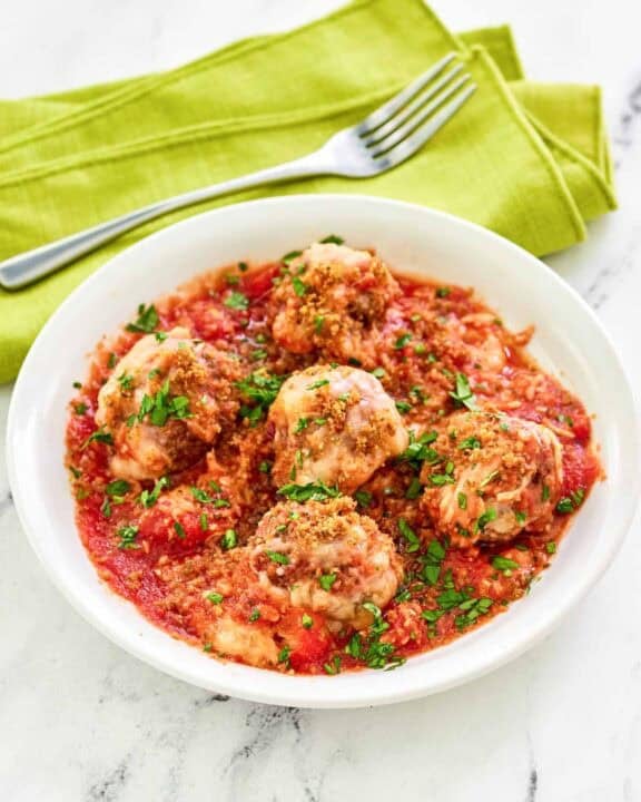 Copycat Olive Garden meatballs parmigiana and a fork on a napkin behind it.