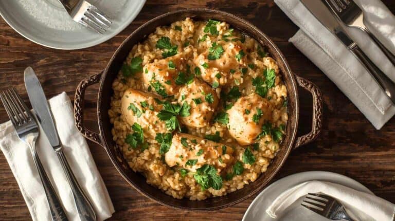 A skillet of creamy chicken and rice garnished with parsley, served family-style.