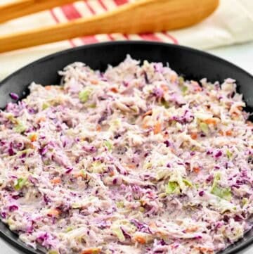 A bowl of copycat Famous Dave's coleslaw and wooden serving tongs behind it.