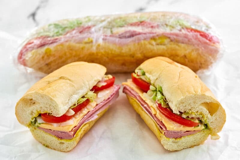 Two copycat Kmart sub sandwiches, one wrapped in plastic and the other cut in half.