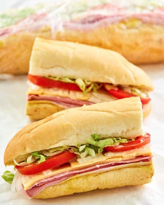Copycat Kmart sub sandwich cut in half and another behind it wrapped in plastic.
