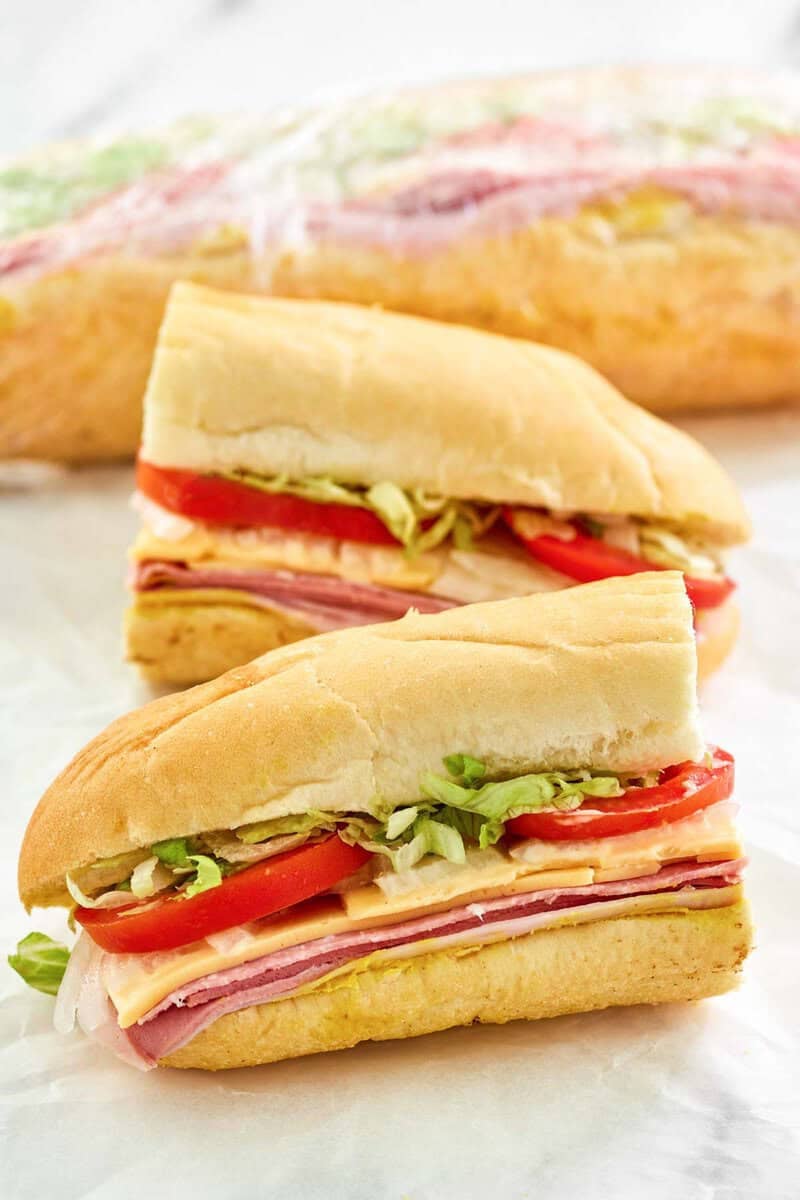 Copycat Kmart sub sandwich cut in half and another behind it wrapped in plastic.