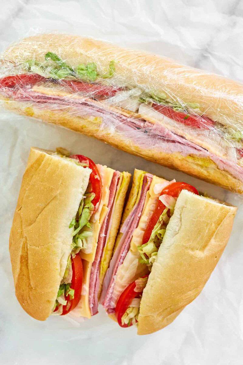 Copycat Kmart sub sandwich wrapped in plastic wrap and one cut in half beside it.