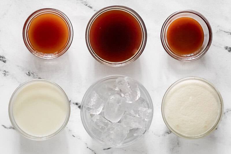 Six glass bowls show the ingredients for a  McDonald's caramel frappe: coffee, caramel syrup, milk, ice, and a creamy base, seen from above.