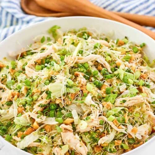 Copycat Ming's Thai chicken salad in a serving bowl and wooden salad servers behind it.