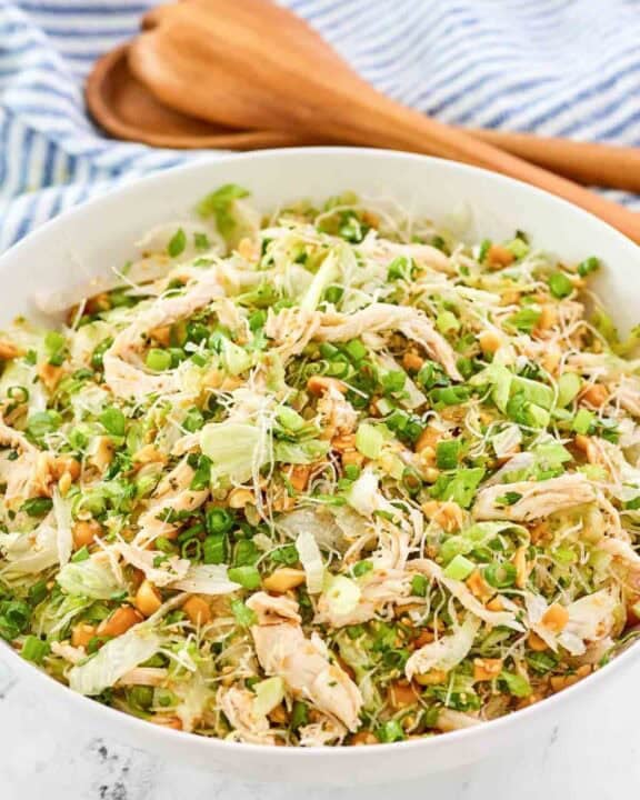 Copycat Ming's Thai chicken salad in a serving bowl and wooden salad servers behind it.