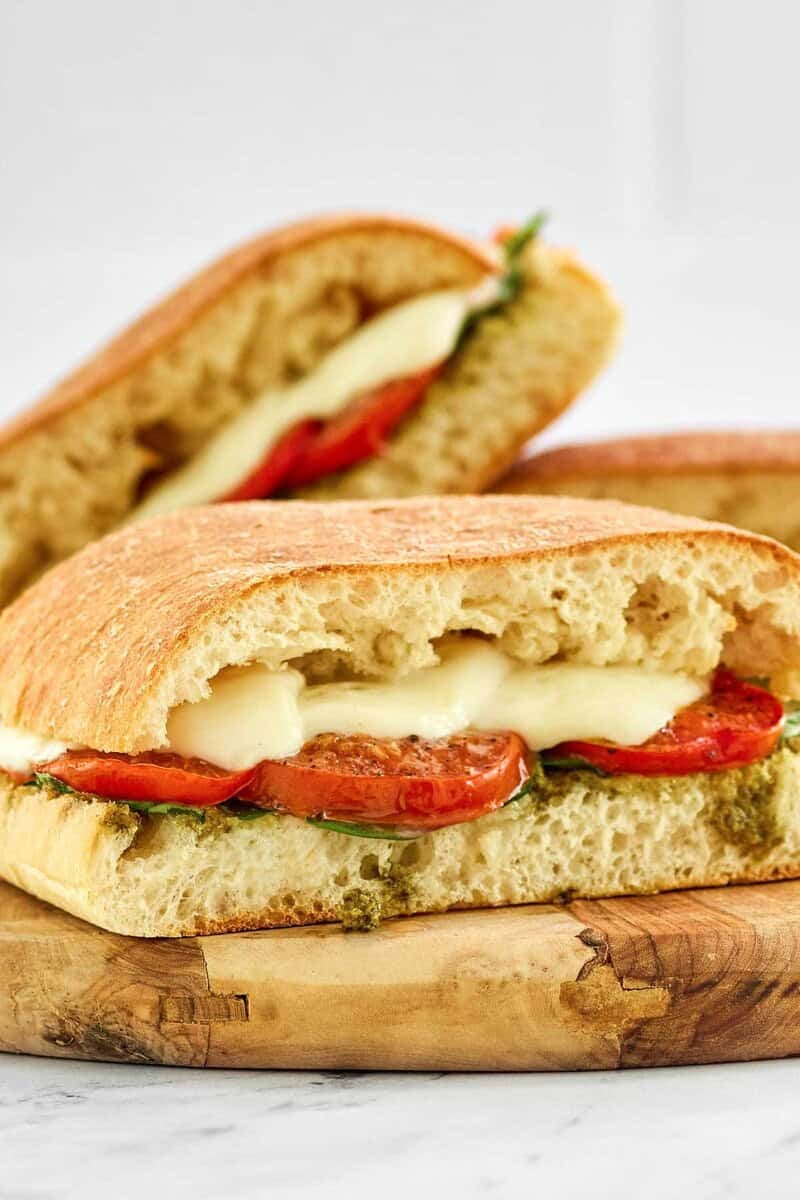 Three copycat Starbucks Tomato and Mozzarella sandwiches are displayed on a wooden cutting board after being toasted.