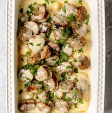Creamy alfredo sausage and gnocchi bake in a casserole dish on a marble surface.