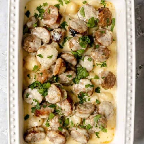 Creamy alfredo sausage and gnocchi bake in a casserole dish on a marble surface.
